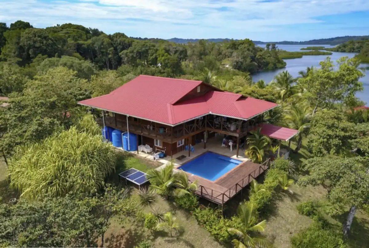 Aerial view of the main hacienda, two-story with red roof, pool, and deck overlooking the water