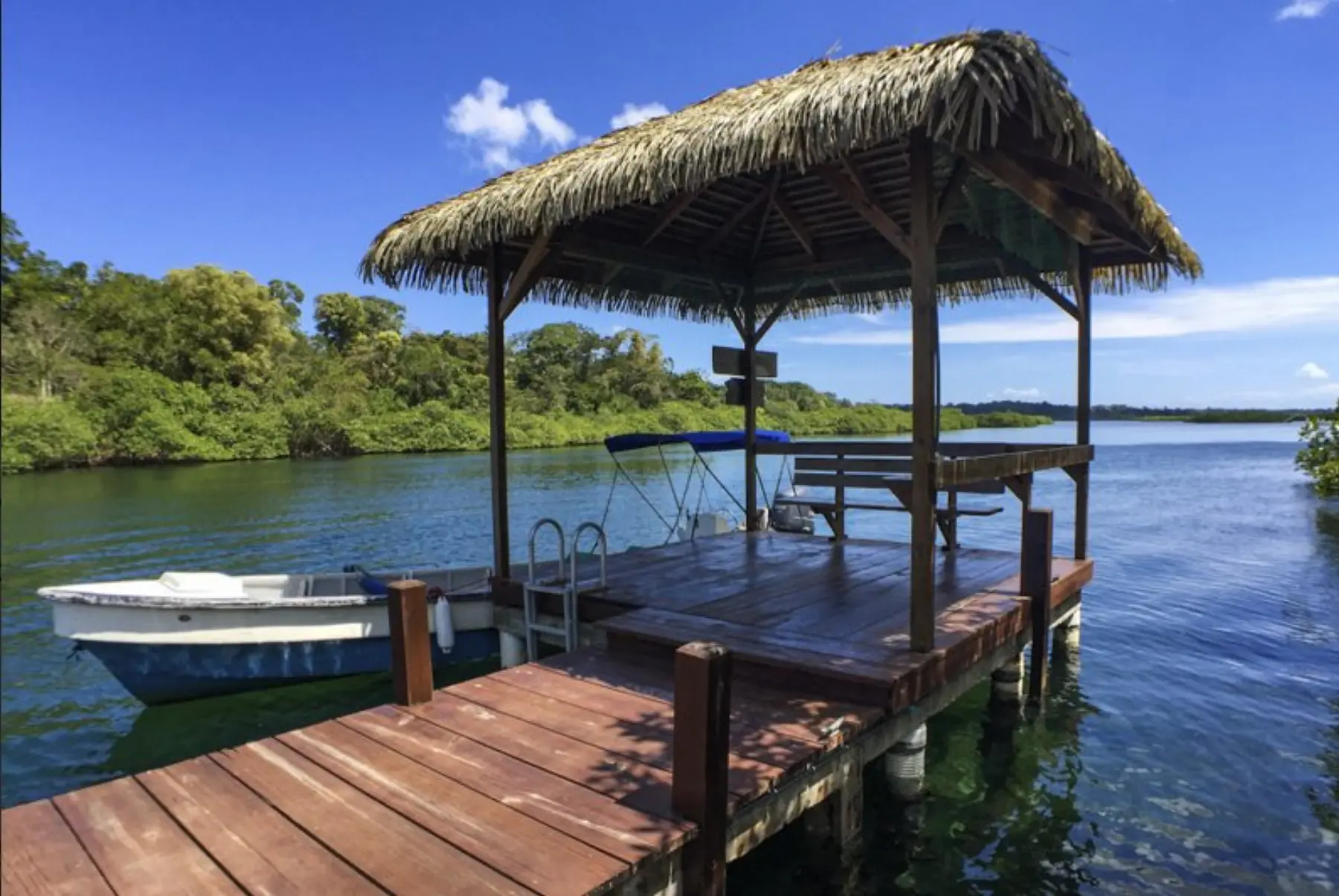 A wooden dock with a thatched-roof boat house and a small boat tied up